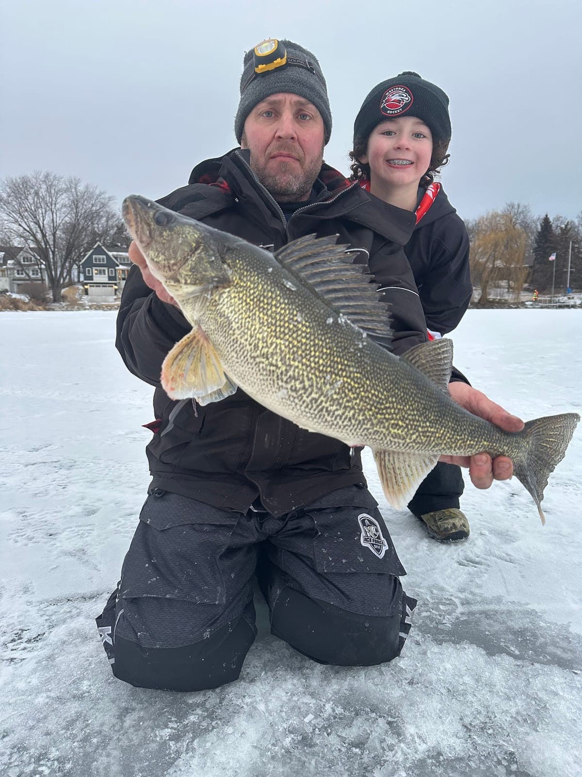 A father and son kneeling on the ice with a big walleye